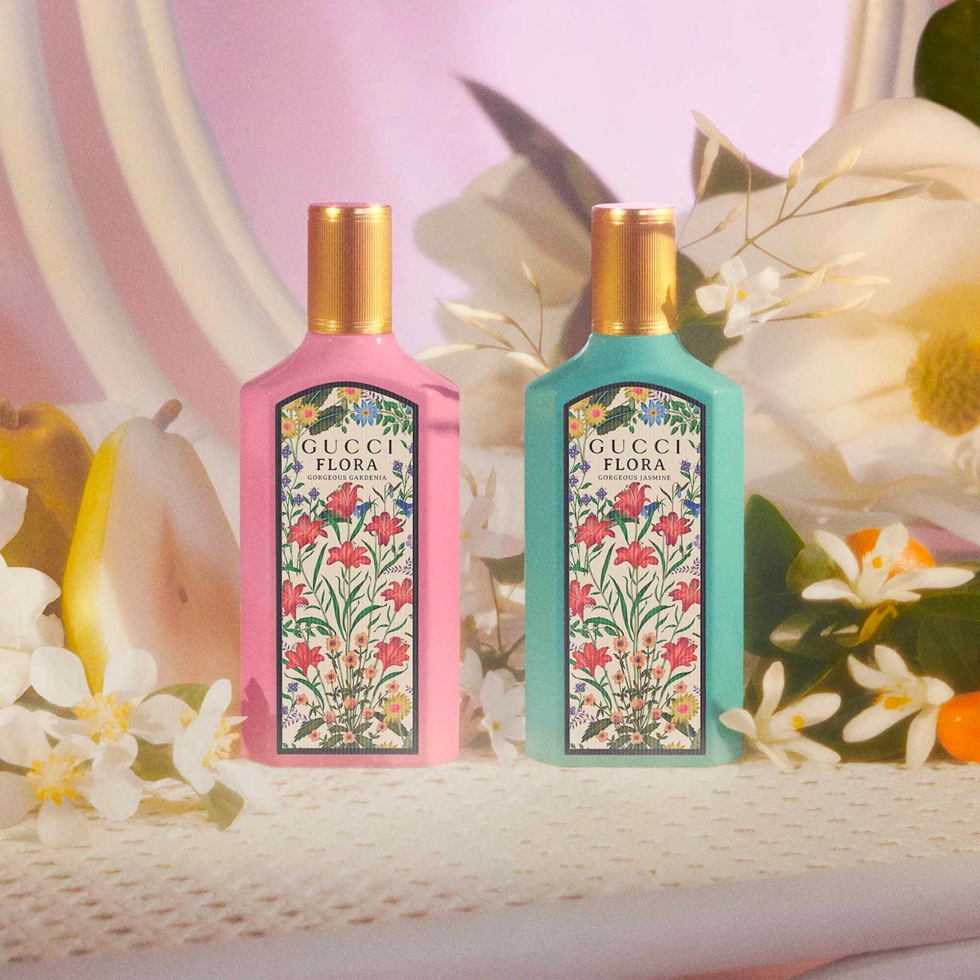 Two Gucci Flora perfume bottles with floral designs on a decorative background with flowers and fruits.
