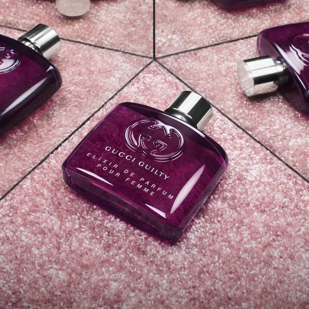 Purple Gucci perfume bottle on a pink glittery surface