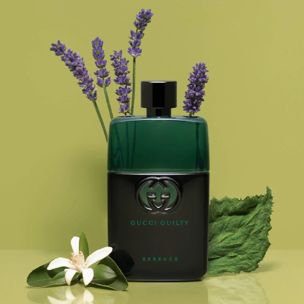 Gucci Guilty Essence perfume bottle with lavender and green leaves on a green background