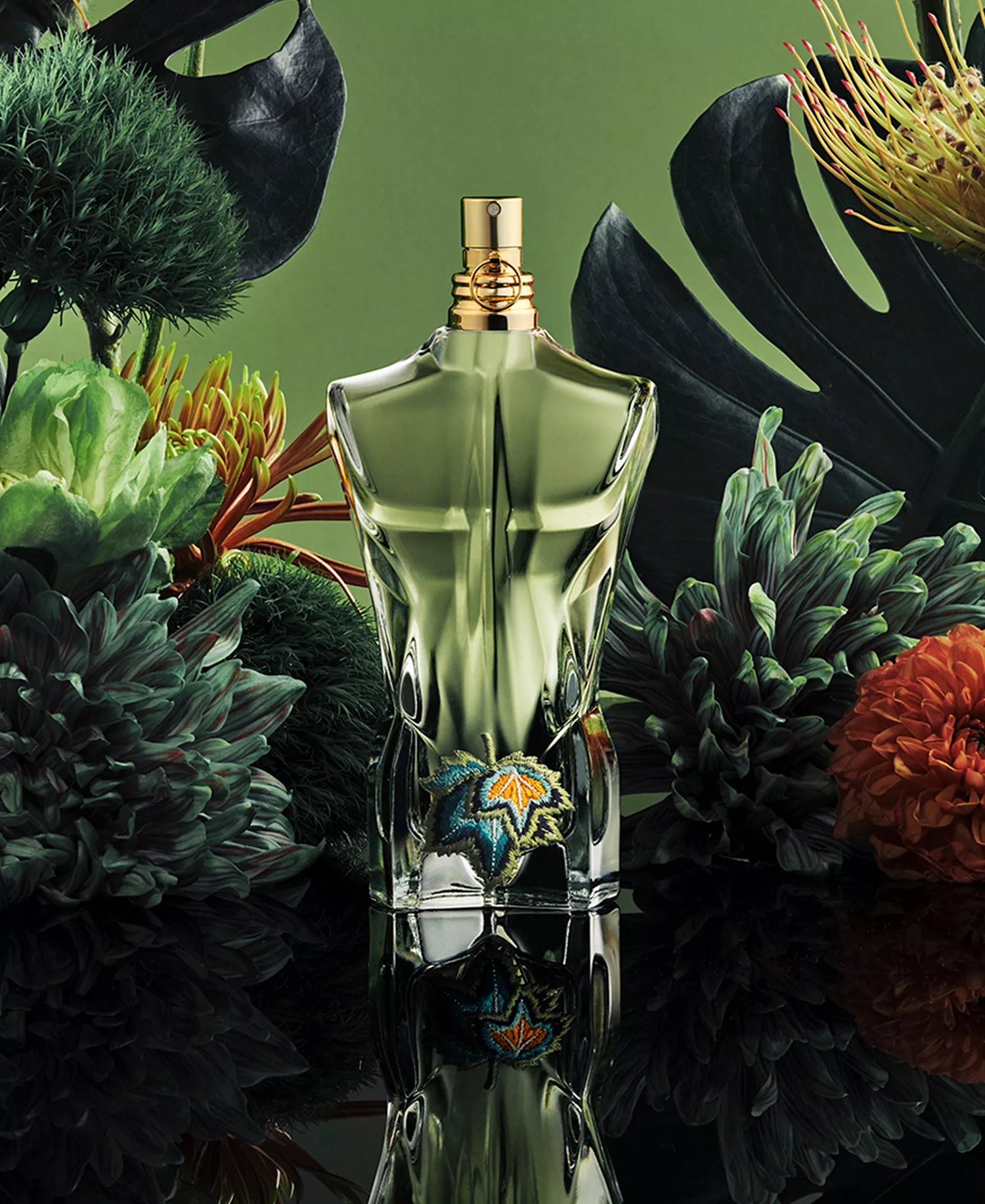 Jean Paul Gaultier Le Beau Paradise Garden EDP in green torso bottle with embroidered leaf emblem surrounded by tropical flowers and monstera leaves