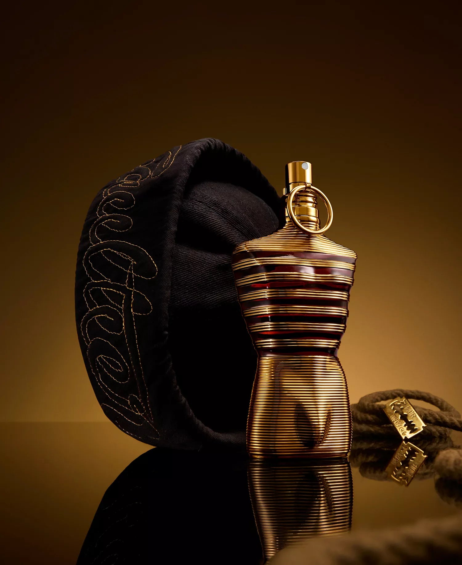 Jean Paul Gaultier Le Male Elixir cologne in gold ribbed bottle displayed with black sailor beret and nautical rope