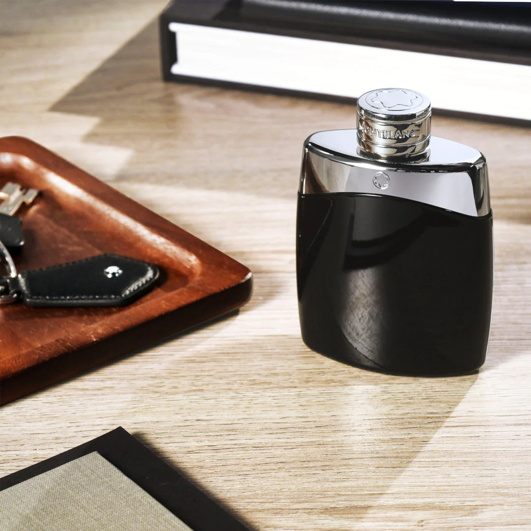 Black and silver perfume bottle on a wooden surface with a keychain and book in the background