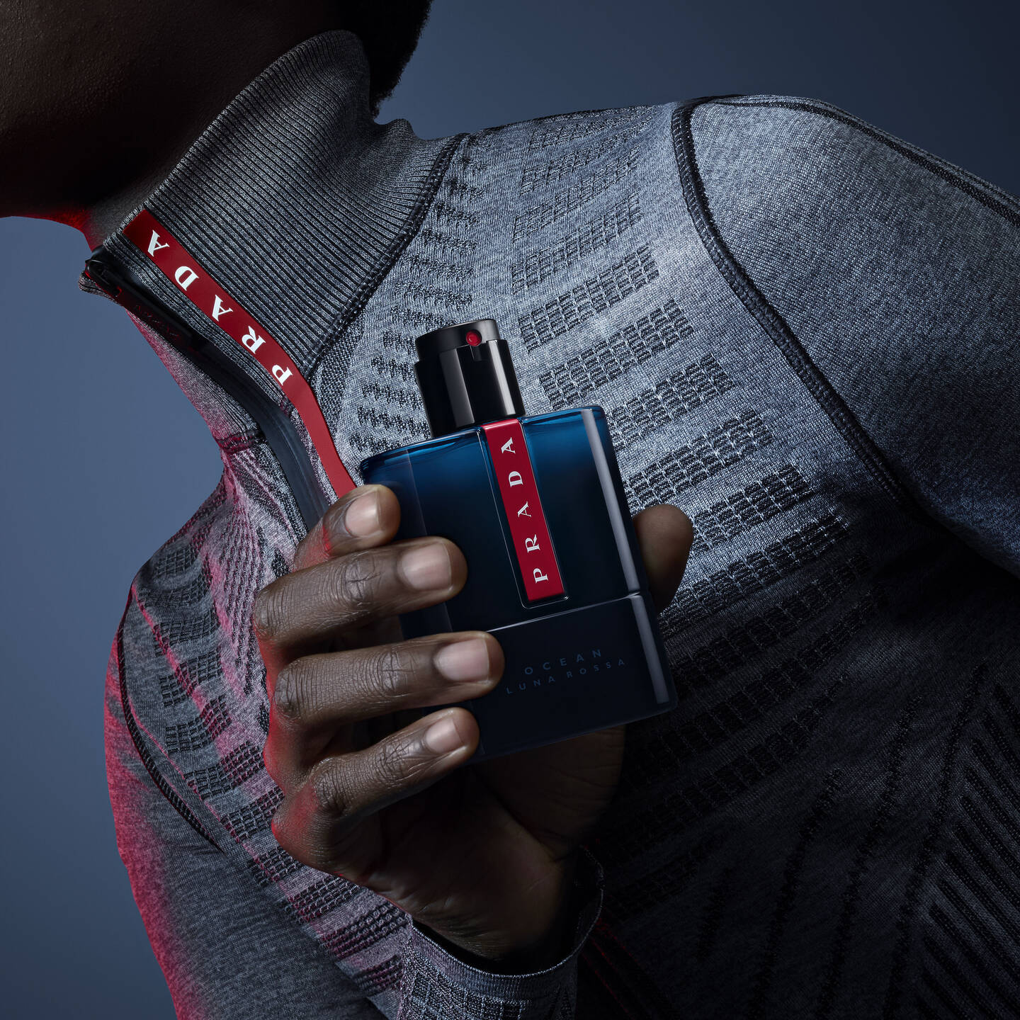 Person holding a Prada perfume bottle against a dark background