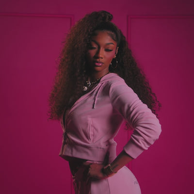 Model in pink tracksuit posing against a magenta background, representing the bold and stylish vibe of Viva La Juicy - Aromatick women's fragrance.