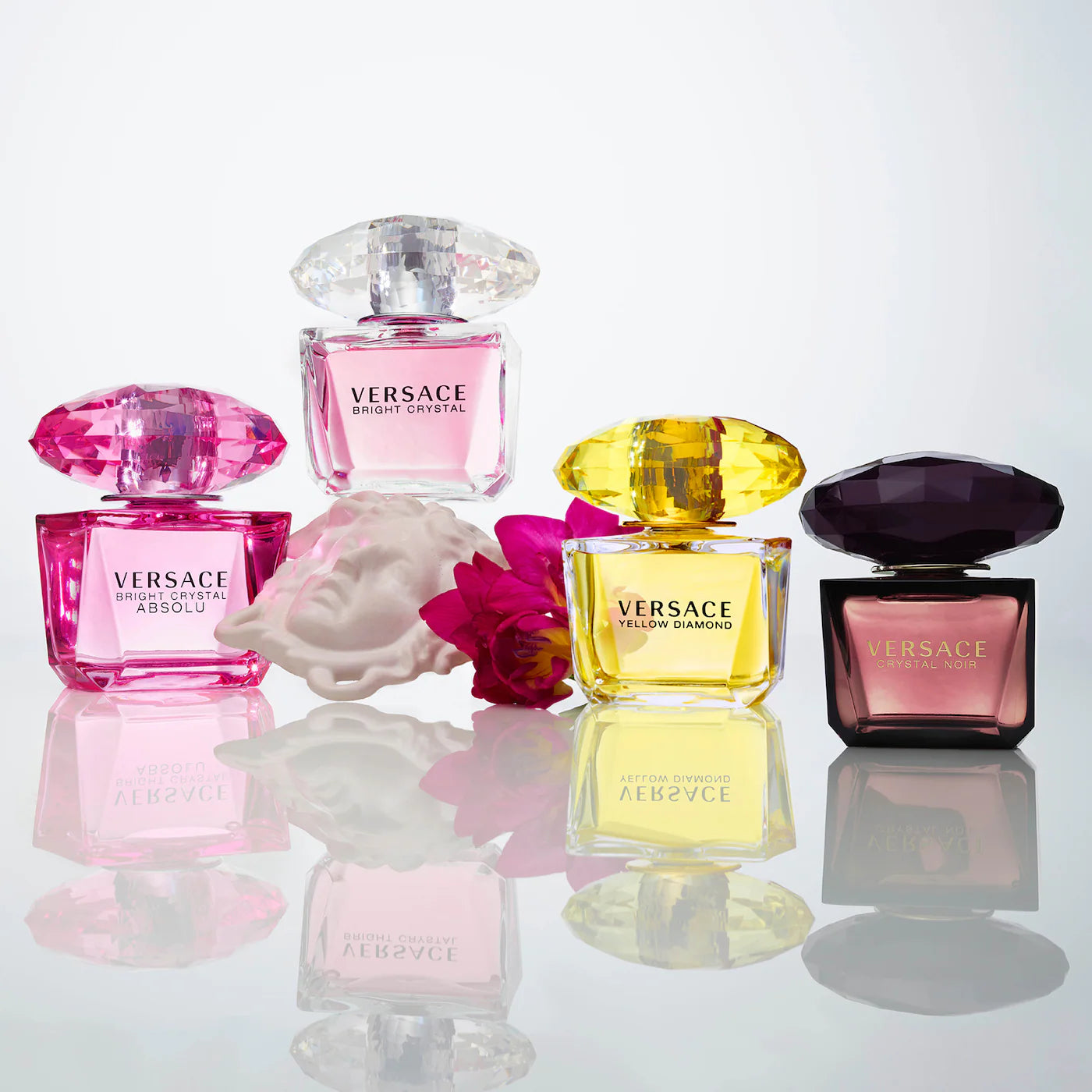 Versace perfume collection with pink Bright Crystal Absolu, yellow Yellow Diamond, and black Crystal Noir bottles displayed with shell and flowers