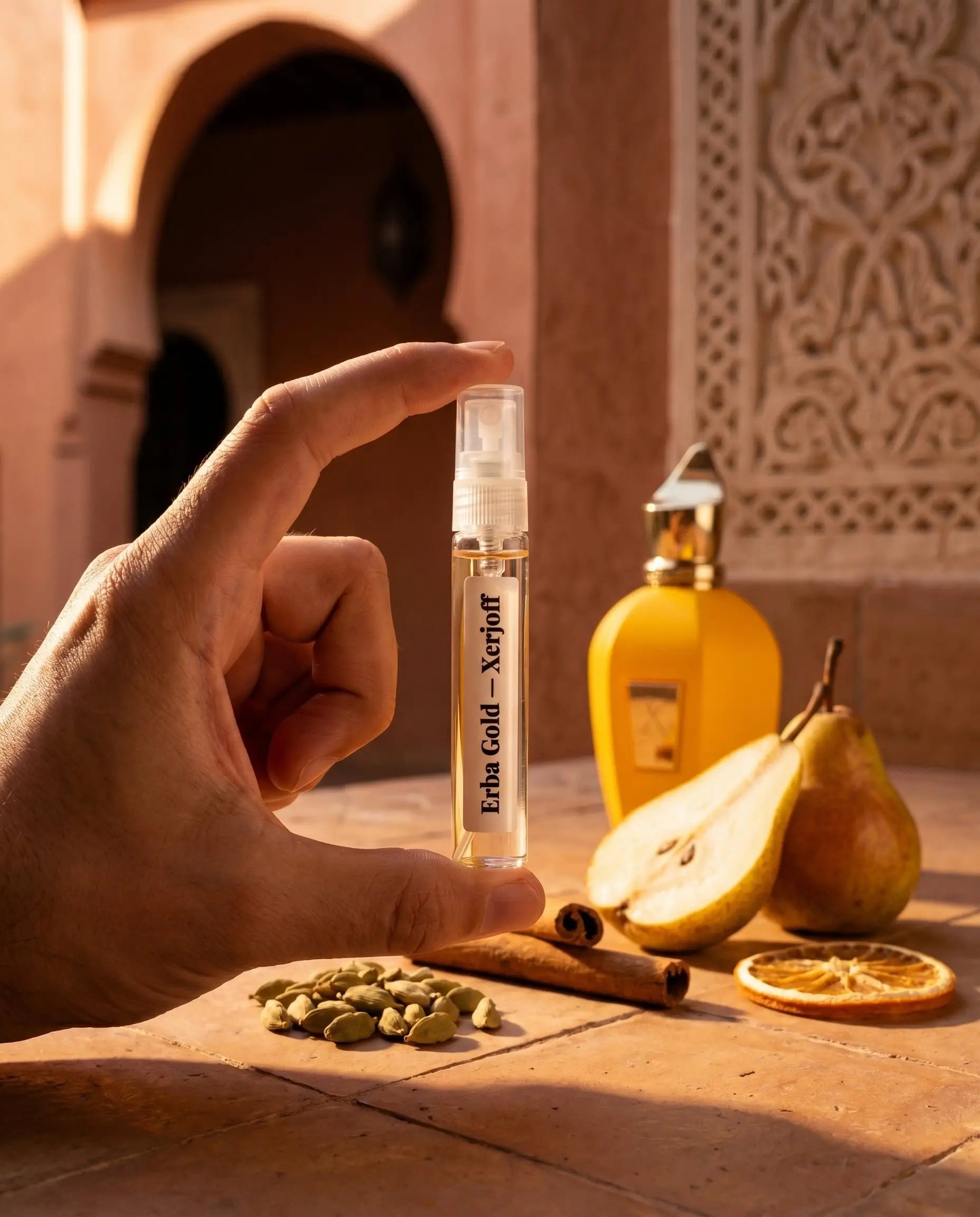 Xerjoff Erba Gold decant vial held in Moroccan riad courtyard with cardamom cinnamon pear and terracotta props