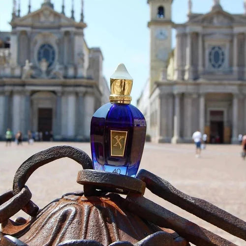 Blue perfume bottle with gold cap on a metal bench in front of a historic building