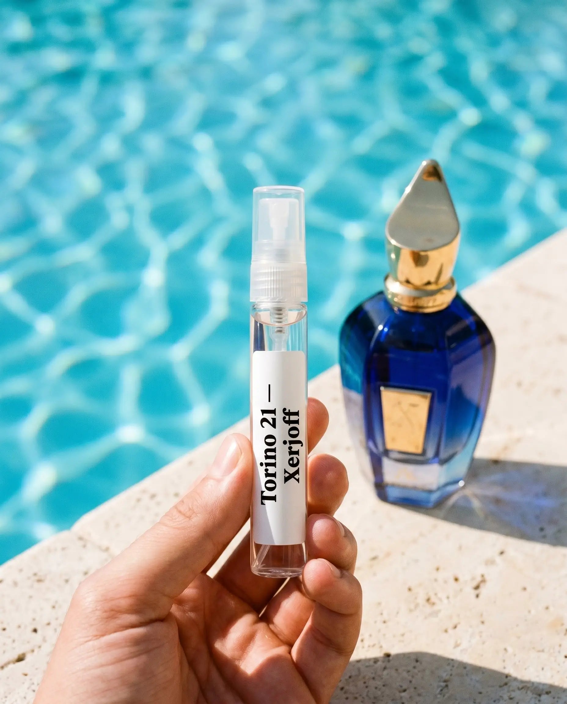 Xerjoff Torino 21 decant vial held at luxury poolside with cobalt blue retail bottle on travertine
