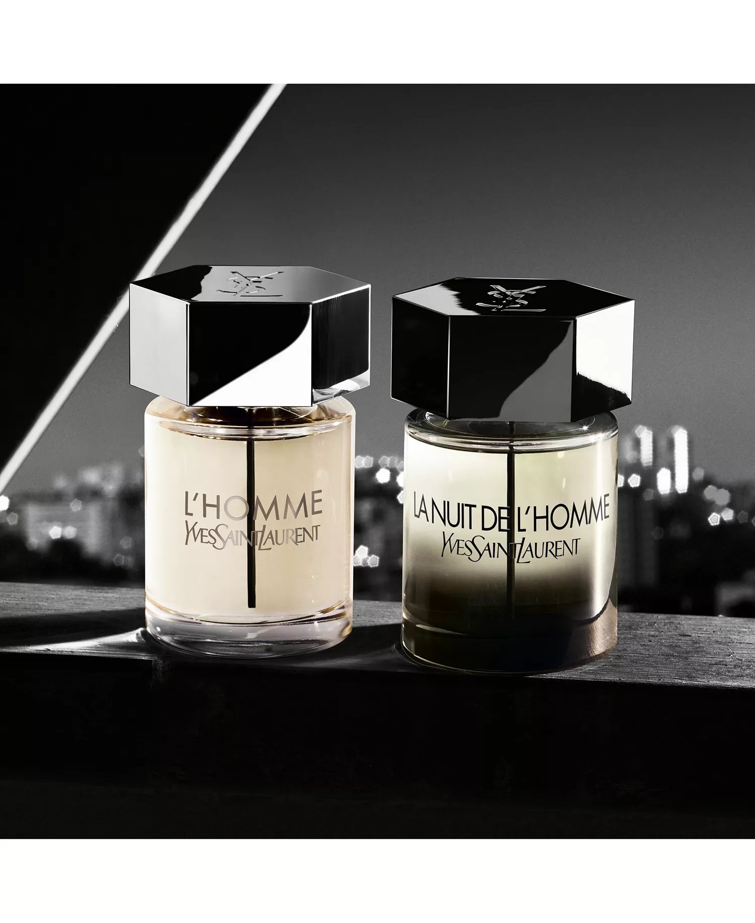 Two Yves Saint Laurent men's fragrances on a reflective surface with a cityscape background