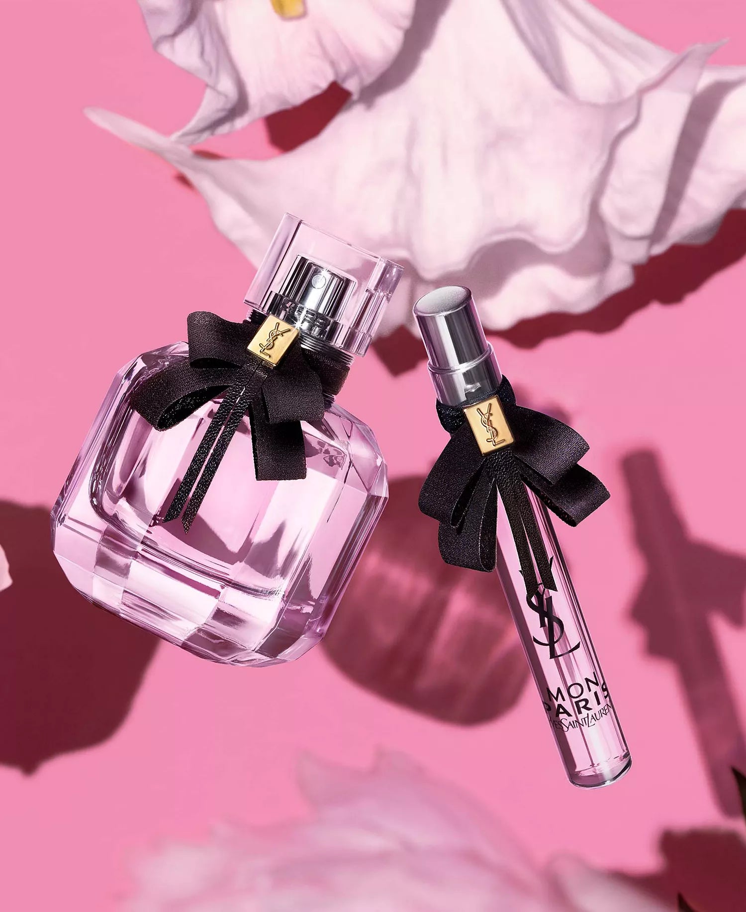 Two perfume bottles with black bows on a pink background