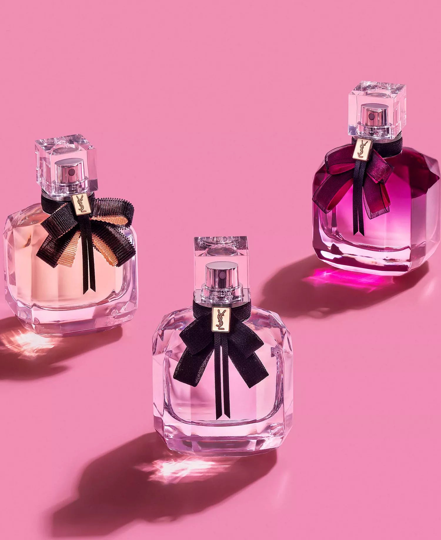 Three perfume bottles with black bows on a pink background