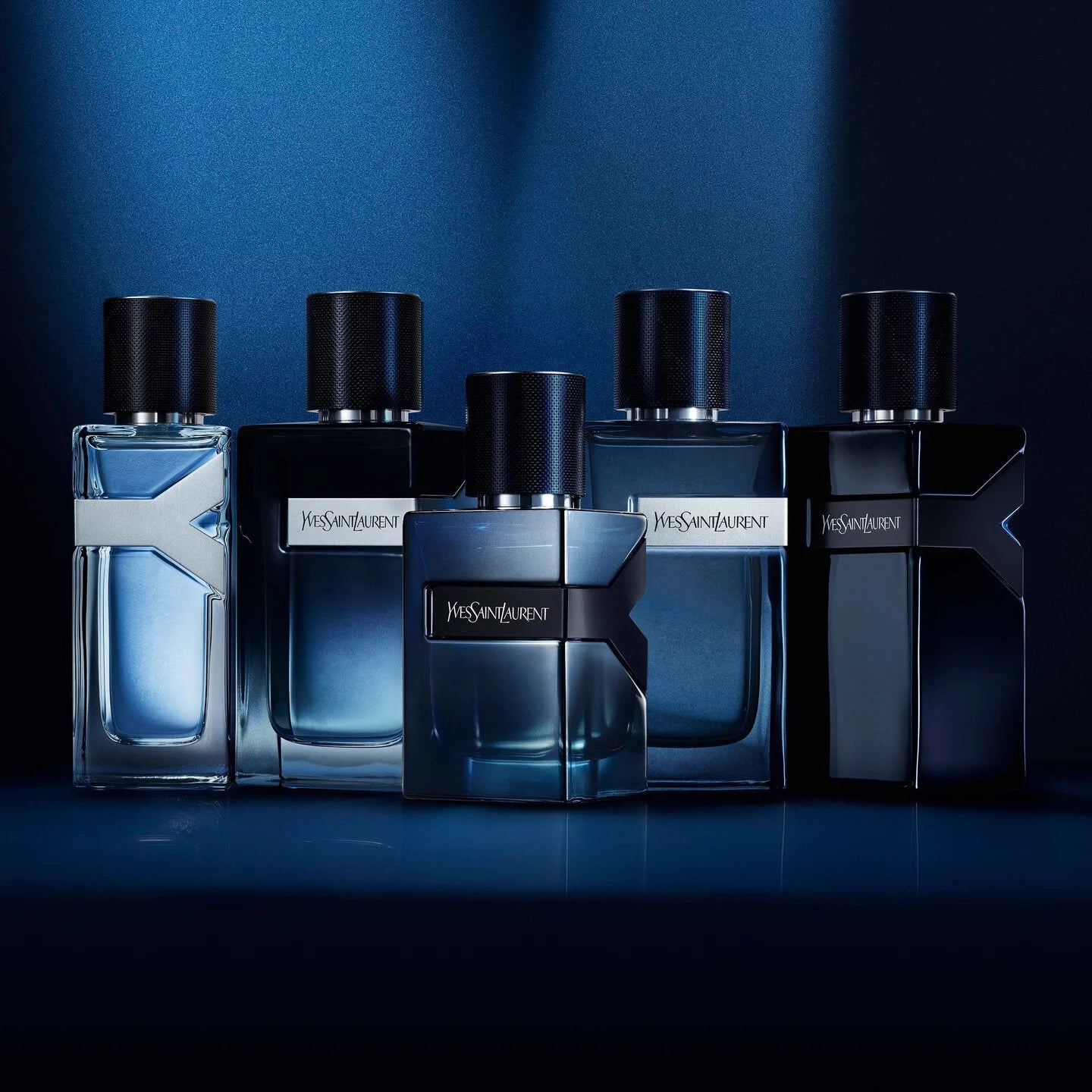 Five Yves Saint Laurent perfume bottles arranged in a row against a blue background